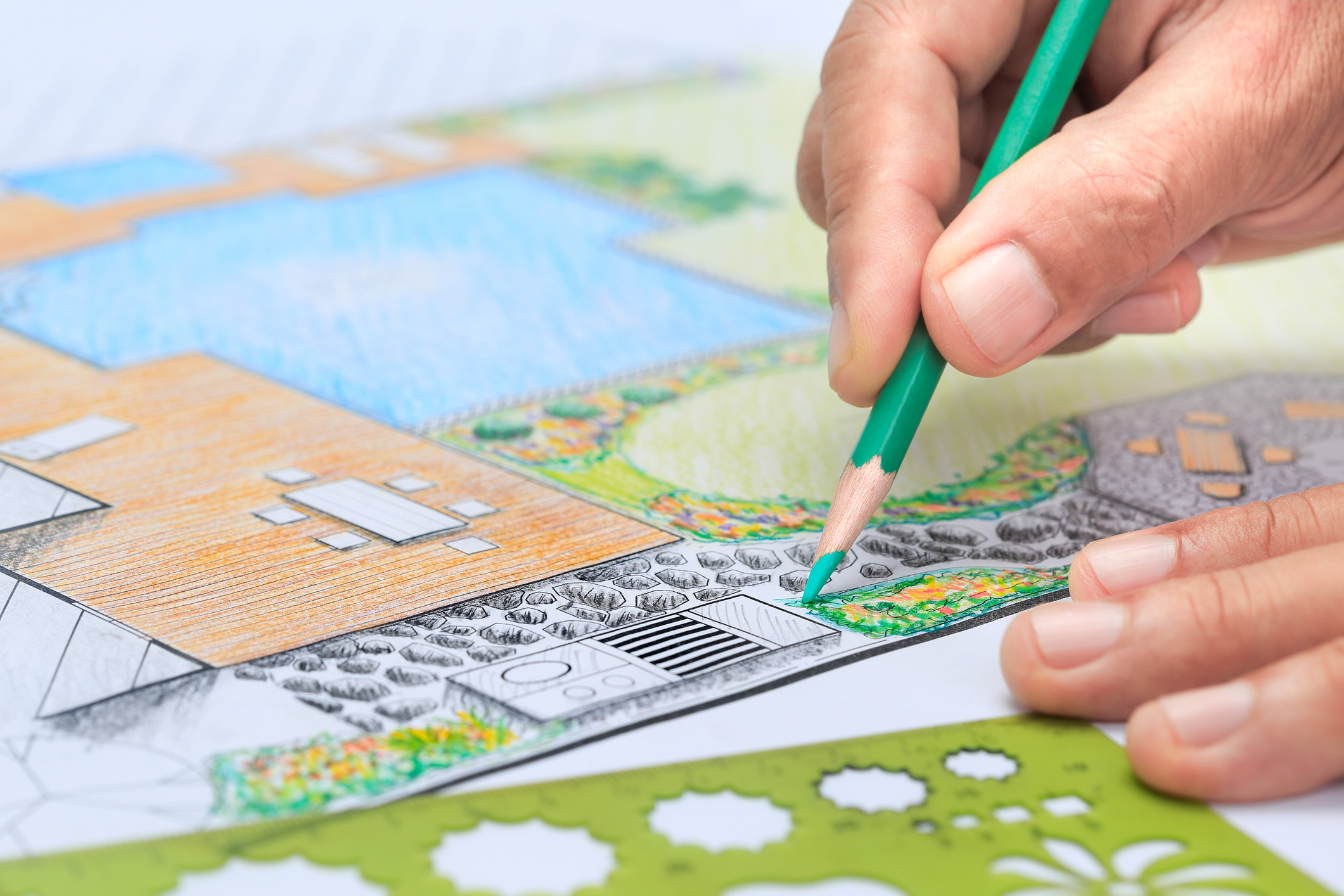 Close-up of a hand holding a pencil over a colorful landscape design blueprint.